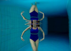 Una ragazza in una piscina ripresa da sott'acqua. Si ha il corpo sommerso e se ne vede il riflesso sul pelo dell'acqua