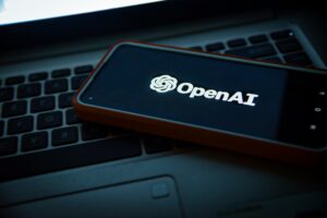 Immagine scura di un cellulare con schermata di sfondo nera e la scritta "OpenAI" con il suo logo.