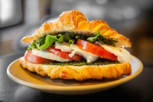 Immagine di un panino fatto con un croissant, farcito con fette di mozzarelle alternate a fette di pomodoro e dell'insalata.