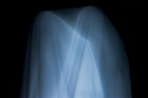 Immagine molto buia, quasi nera, da cui spiccano al centro due riproduzioni di fantasmi ottenute con lenzuola bianche, le due figure sono in trasparenza e si sovrappongono per metà.
