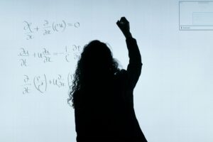 Una donna di spalle, in controluce, che scrive su una lavagna delle formule matematiche