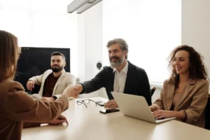 Foto di persone che si stringono la mano attorno a un tavolo. Contesto lavorativo che evoca un accordo siglato.