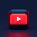 Logo di YouTube in un cubo 3D con gli spigoli arrotondati in un ambiente nero.