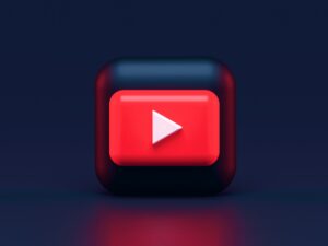 Logo di YouTube in un cubo 3D con gli spigoli arrotondati in un ambiente nero.