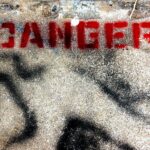 Immagine della dritta "DANGER" in stampatello fatta con la bomboletta rossa su un pavimento d'asfalto.