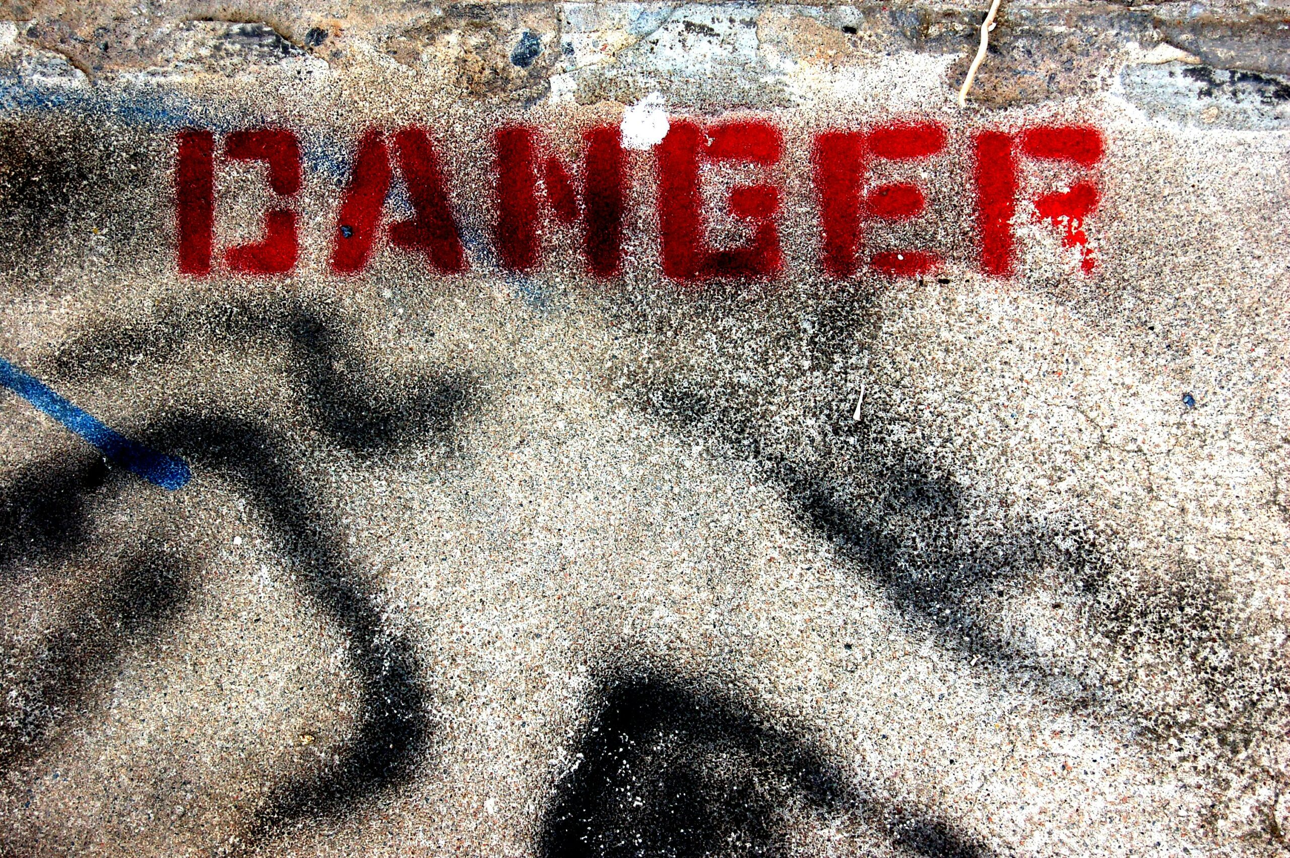 Immagine della dritta "DANGER" in stampatello fatta con la bomboletta rossa su un pavimento d'asfalto.