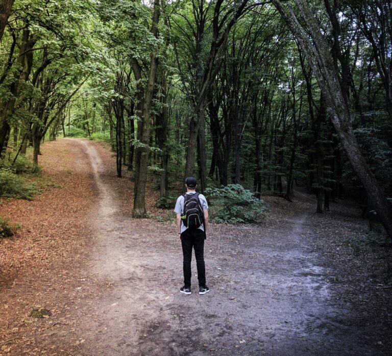 Immagine di un apersona che si ritrova a un bivio tra due sentieri in un bosco.Si ritrova a dover scegliere quale strada intraprendere.